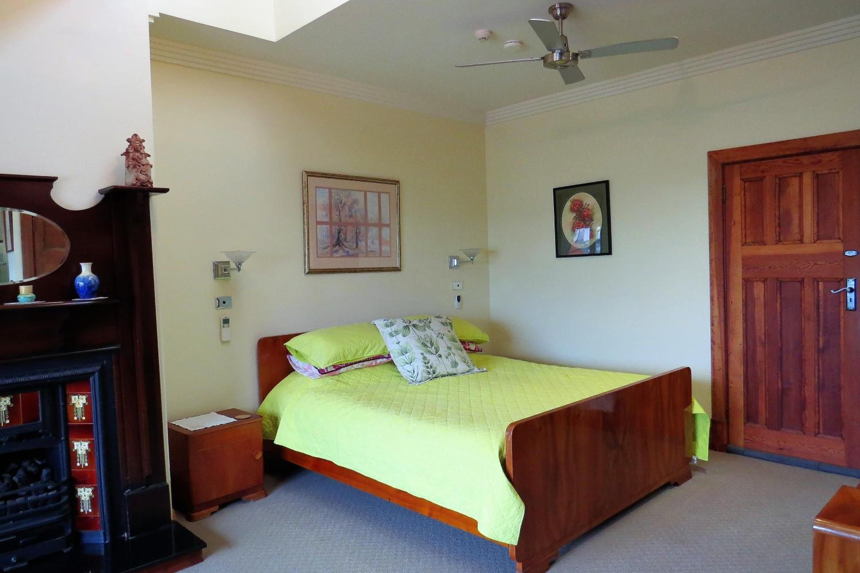 A bedroom with a bed, a nightstand, a dresser, a ceiling fan, and a door.