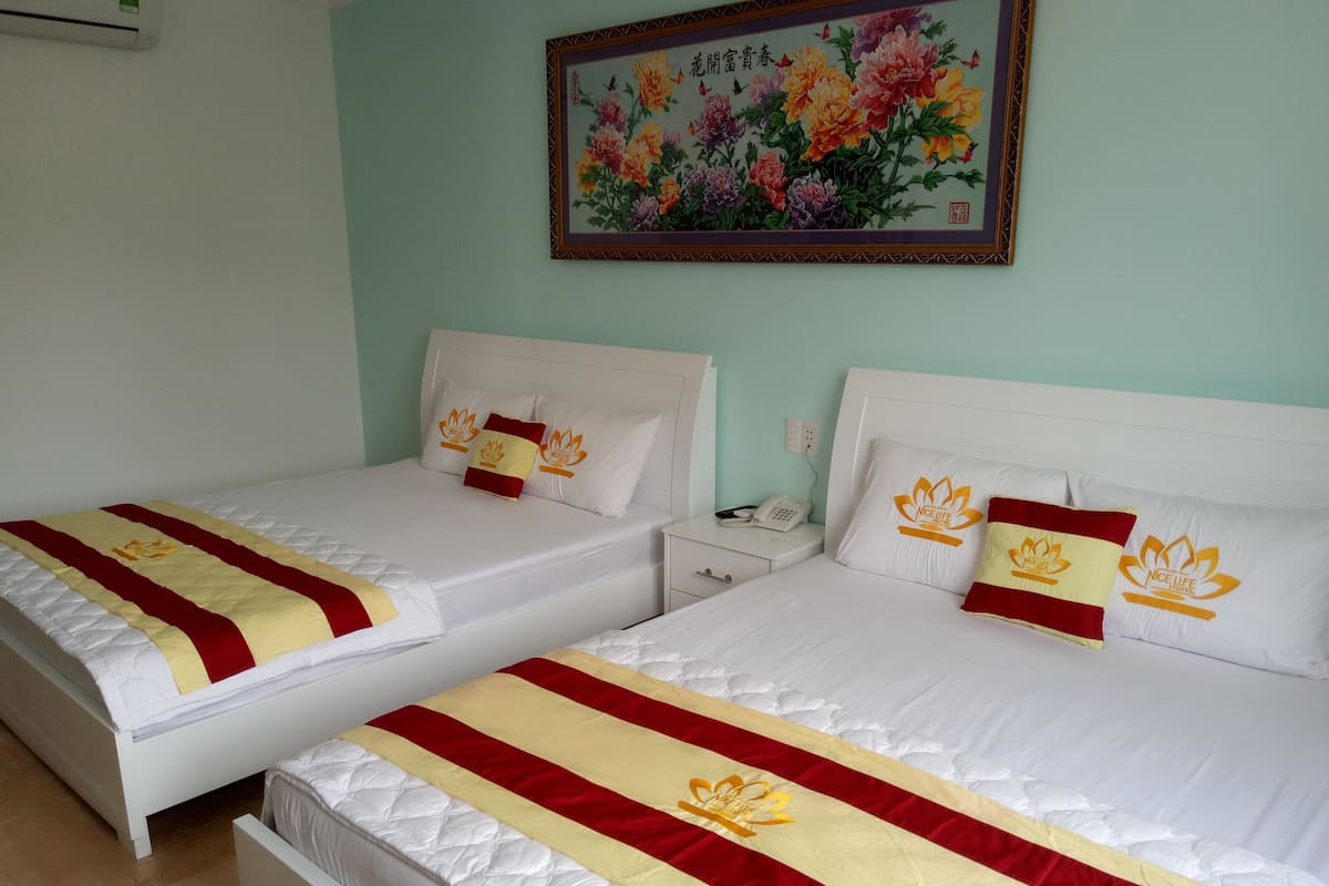 Two twin beds with white headboards and red and yellow bedspreads, a painting of flowers on the wall, and a bedside table with a phone.