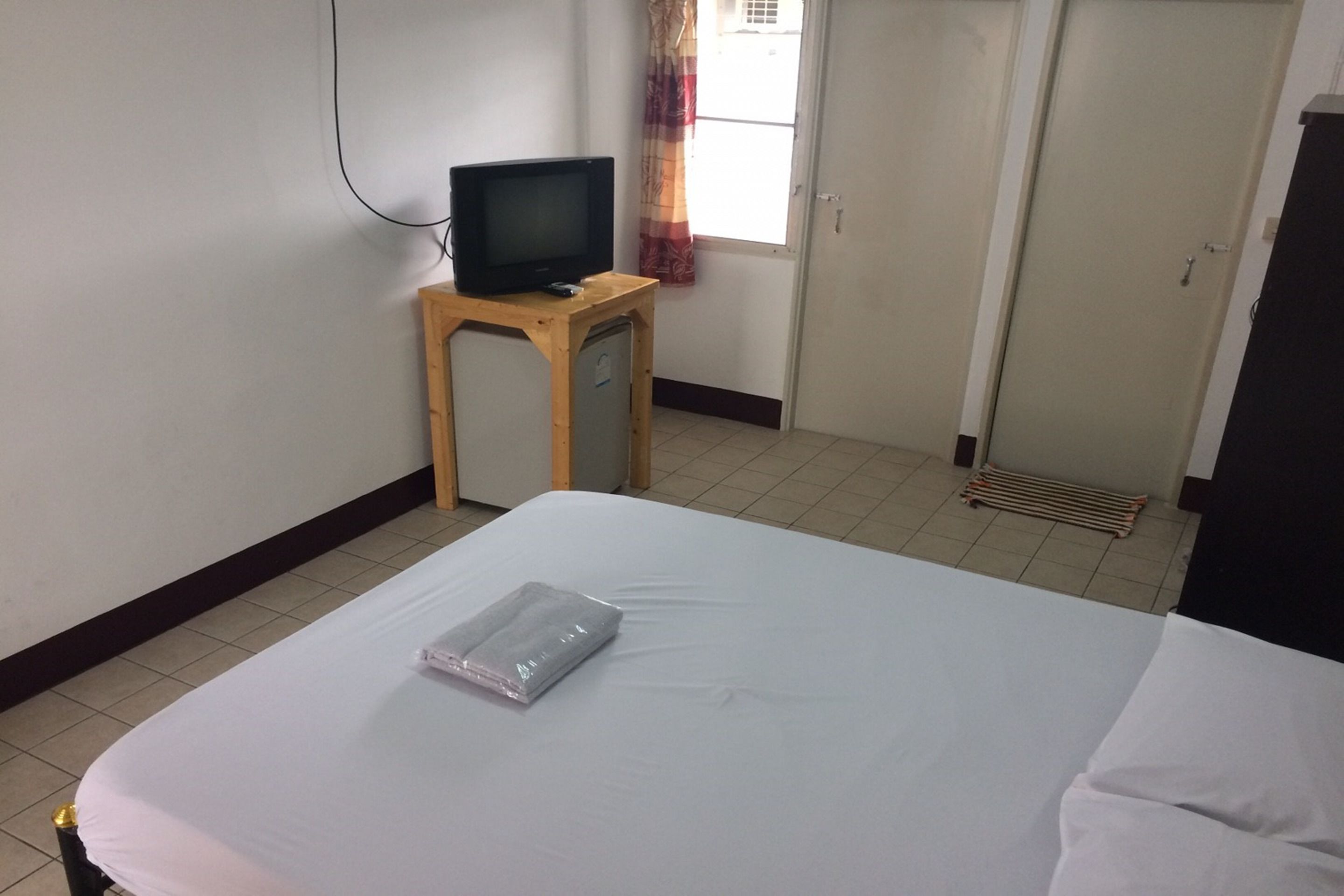 A hotel room with a bed, a television on a wooden stand, a window with curtains, and a door.