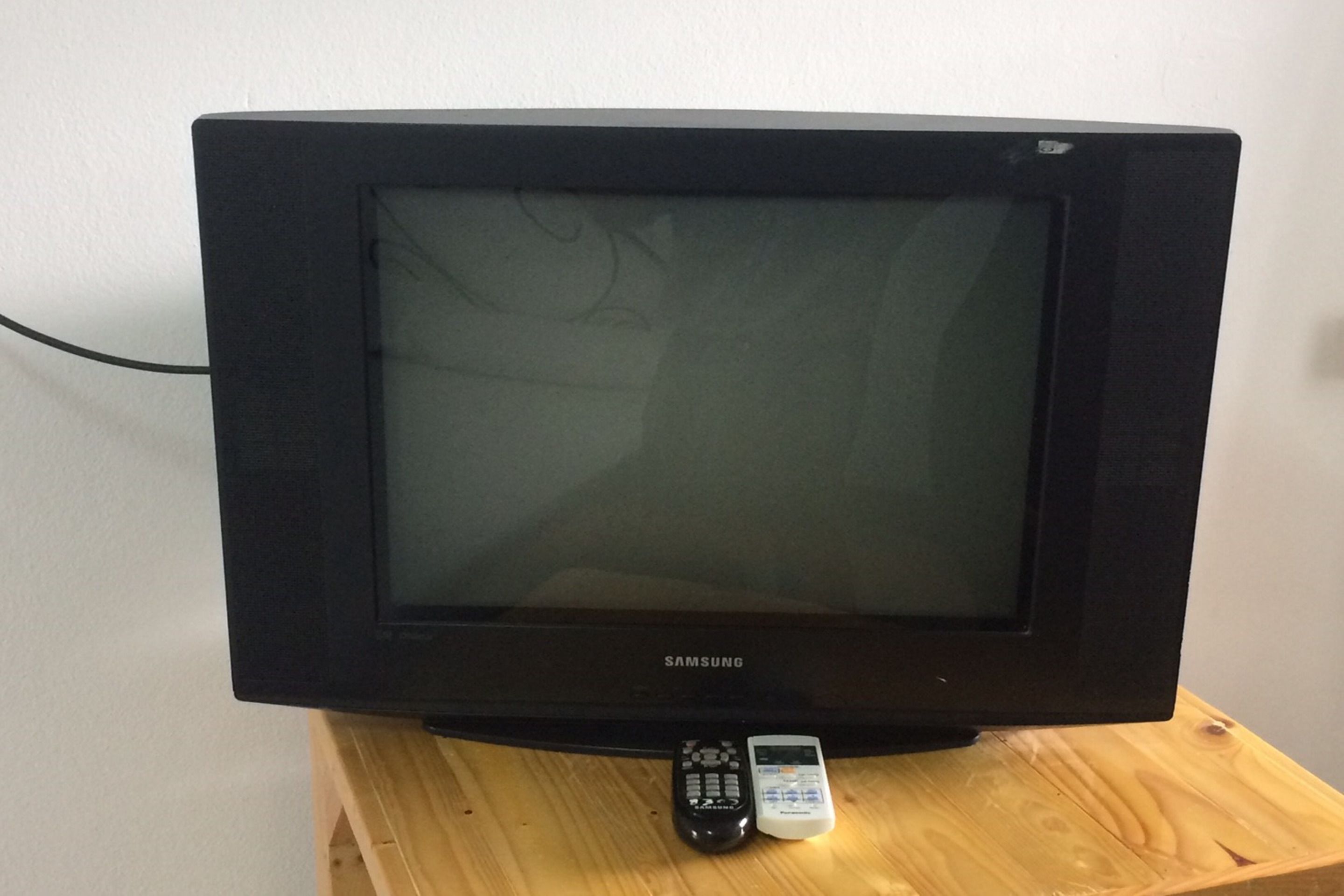 A Samsung television on a wooden stand with a remote control beside it.