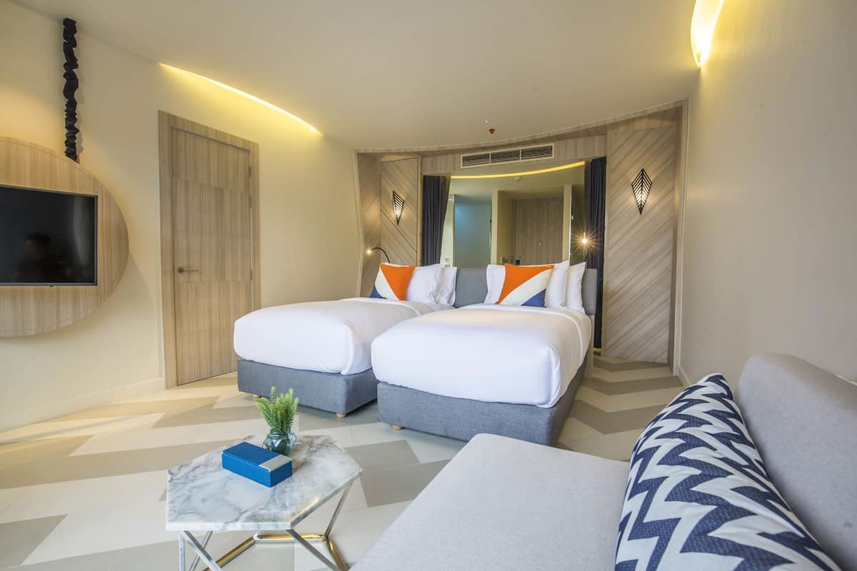Habitación de hotel con dos camas, televisor, una mesita con una planta y un sofá.
