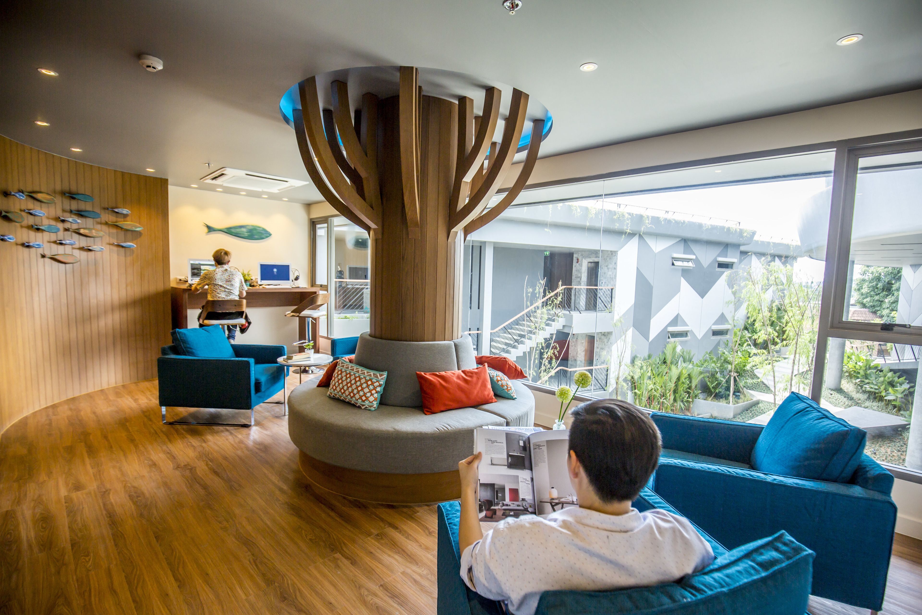 En modern hotellobby med en central träkonstruktion, sittområden och stora fönster som erbjuder utsikt över omgivningarna.