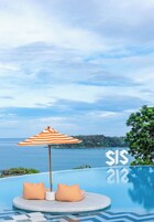 An infinity pool with a view of the sea, striped beach chairs, and an umbrella.
