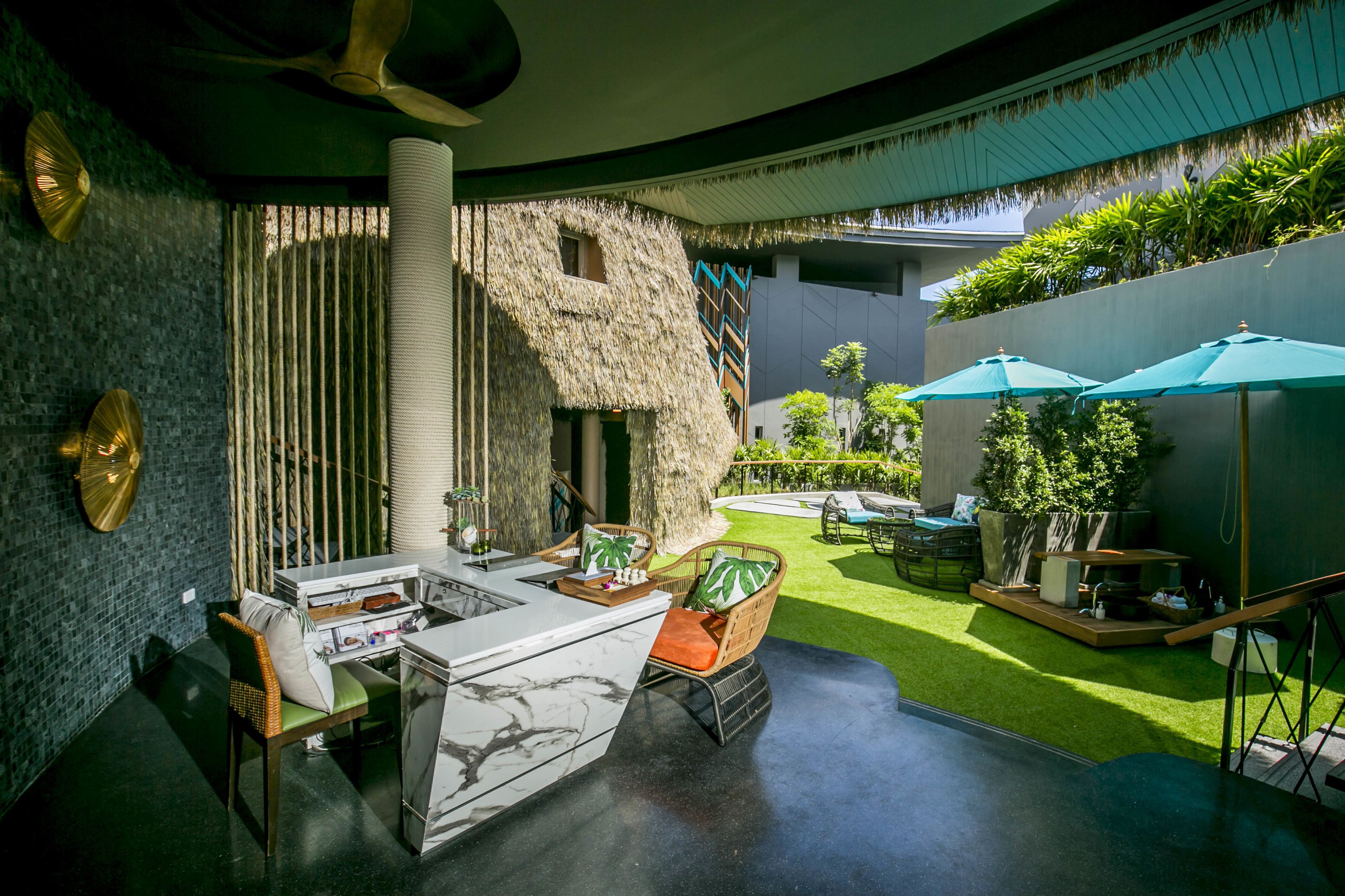 A modern interior with a bar area, a thatched structure, and a green outdoor space with umbrellas.