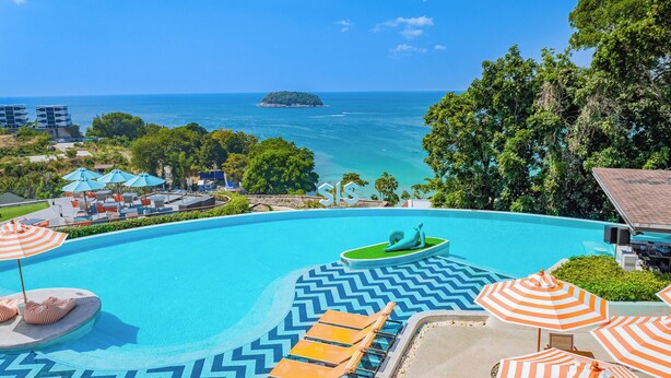 Ein Poolbereich mit Liegestühlen und Sonnenschirmen, Blick auf den Ozean und eine kleine Insel in der Ferne.
