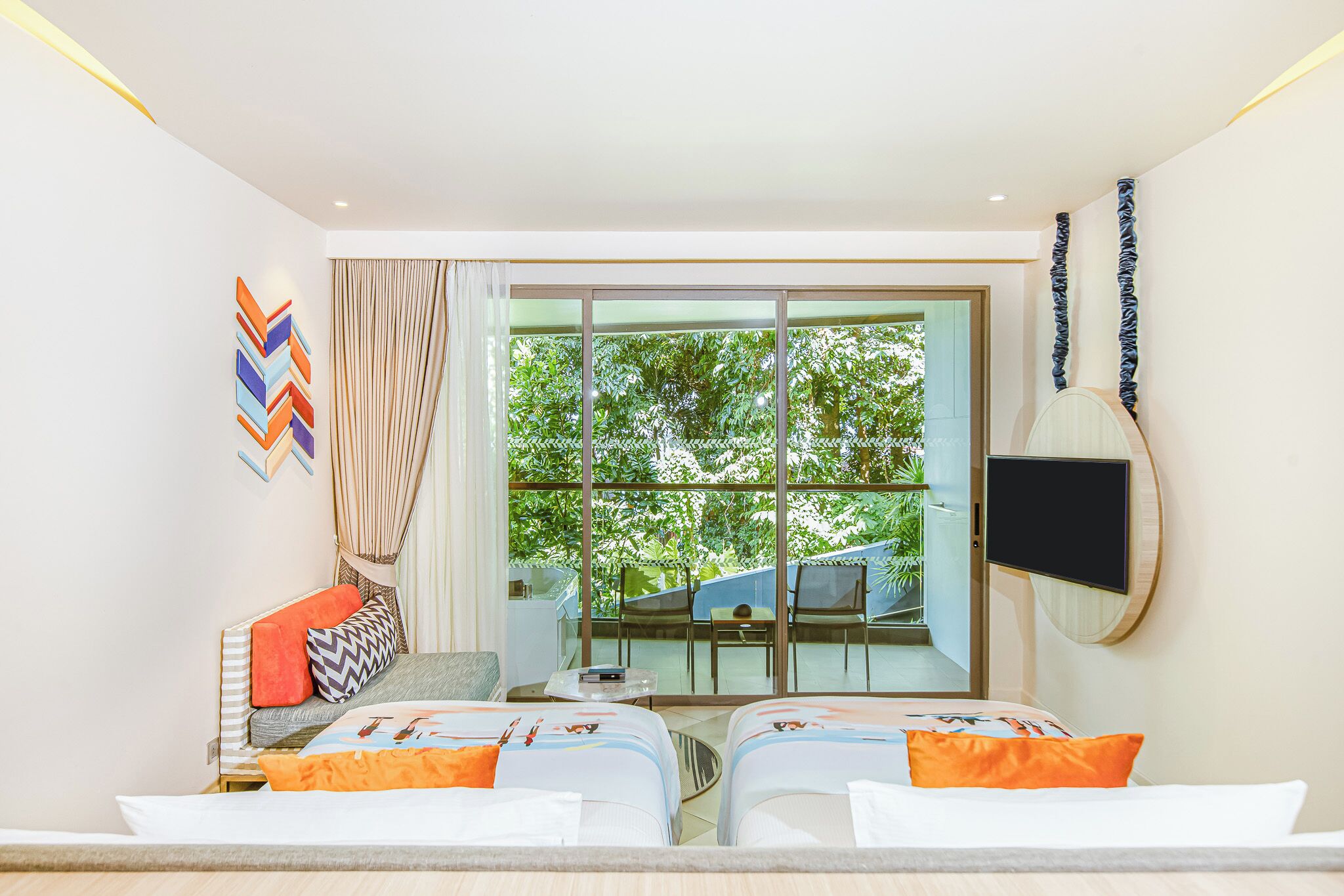 Una habitación de hotel moderna con un amplio ventanal corredero que da a un balcón, un televisor de pantalla plana montado en la pared y una cama con muchas almohadas.