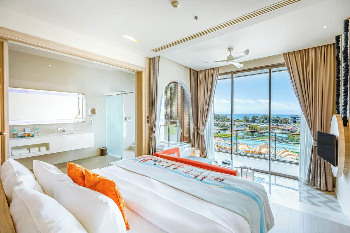 Habitación de hotel moderna con una cama grande, baño y balcón con vistas a una piscina y al complejo turístico.