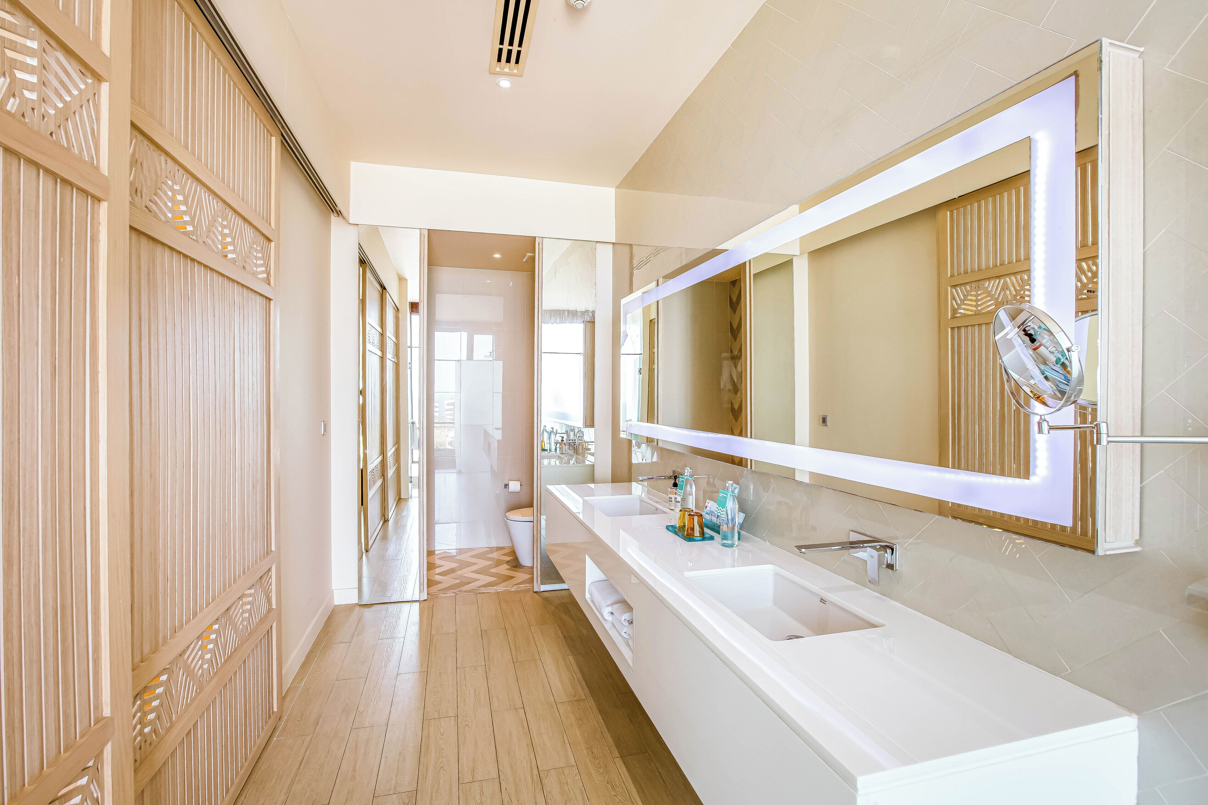 A modern bathroom with a large mirror, two sinks, and a shower area.