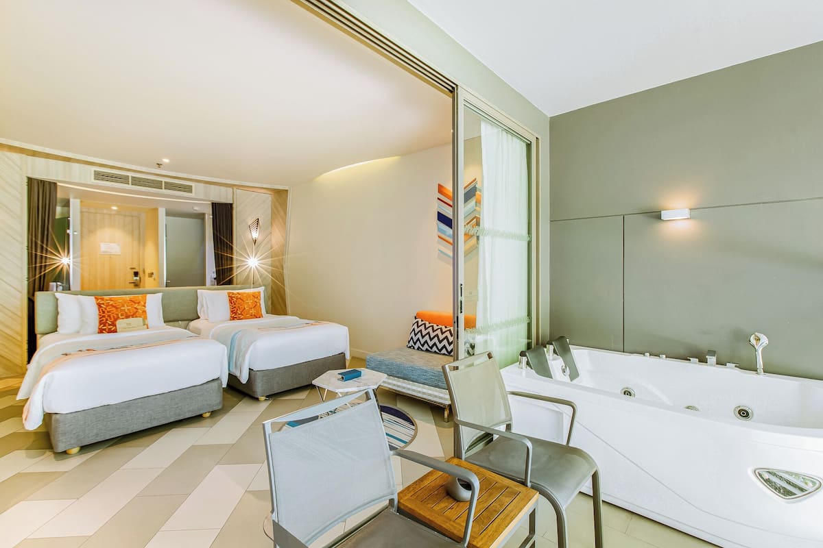 Habitación de hotel moderna con dos camas, una bañera grande y una zona de estar con mesa y sillas.