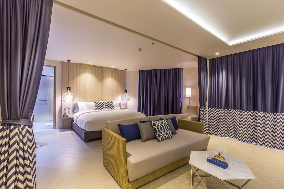 Una habitación de hotel con cama, sofá, mesa de centro y cortinas.