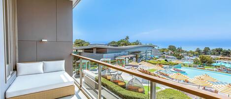 A balcony with a sofa, a pool area with umbrellas, and a view of the sea.