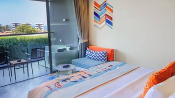 Una habitación de hotel moderna con balcón, cama con colcha colorida, una mesita y una silla.