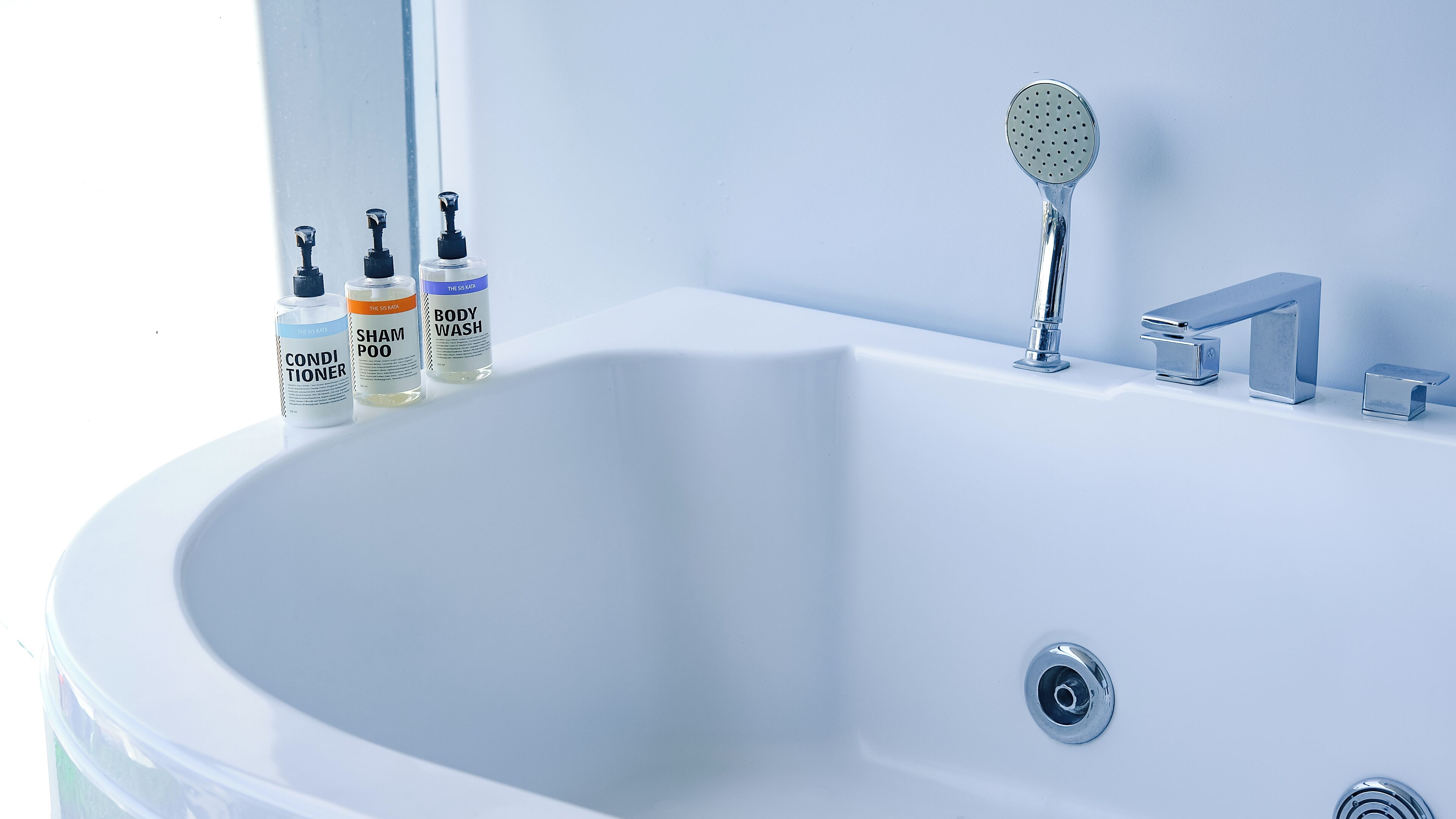 Un bagno moderno con una vasca da bagno bianca, un soffione a mano e tre flaconi di shampoo, balsamo e detergente corpo.