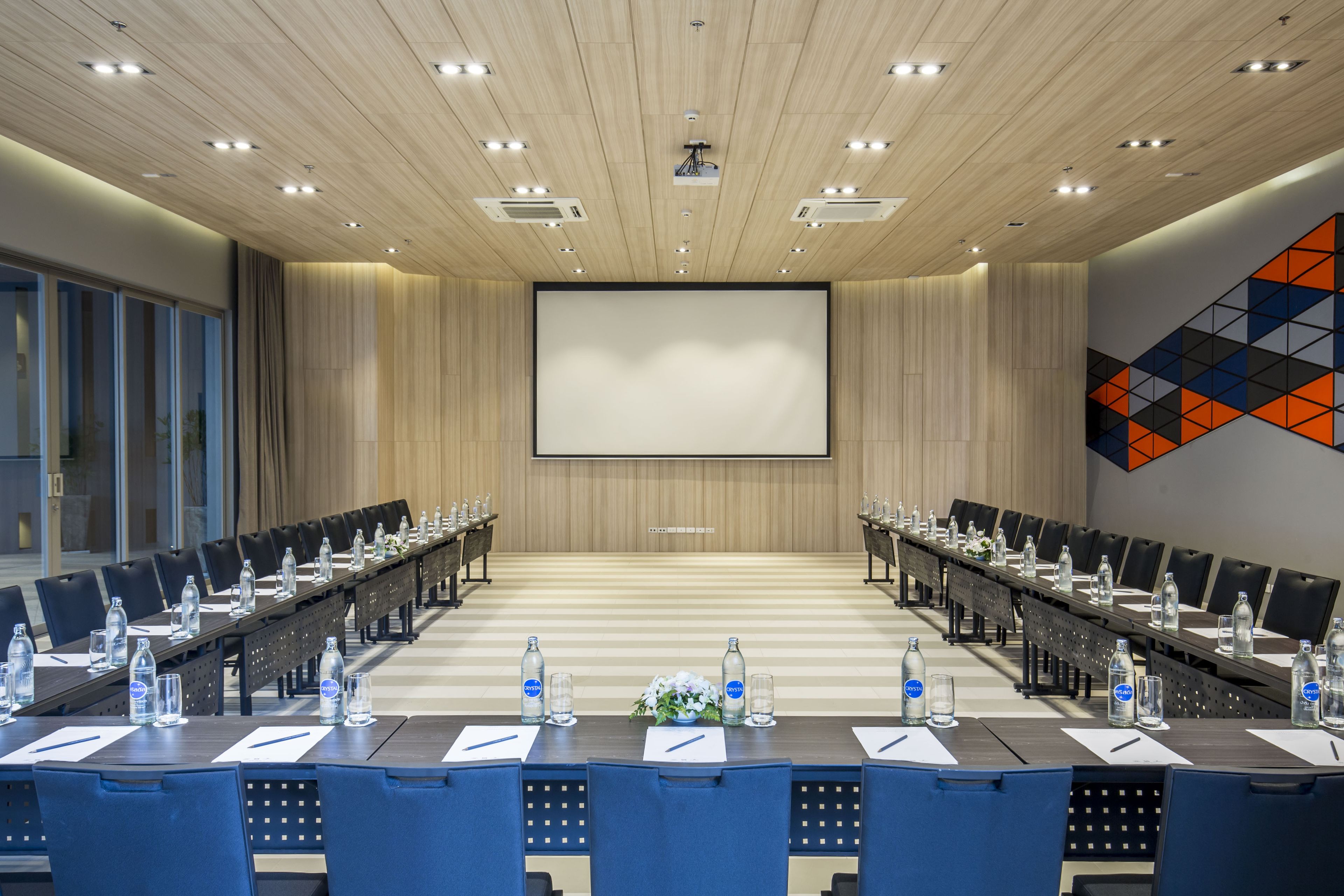 Una sala conferenze con un lungo tavolo, sedie, bottiglie d'acqua e uno schermo per proiettore.