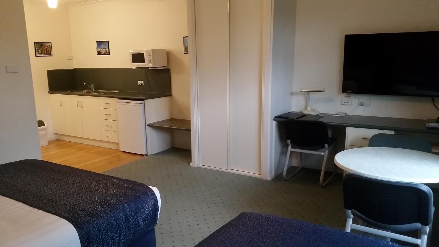 A compact room with a kitchenette, a bed, a desk, and a TV.