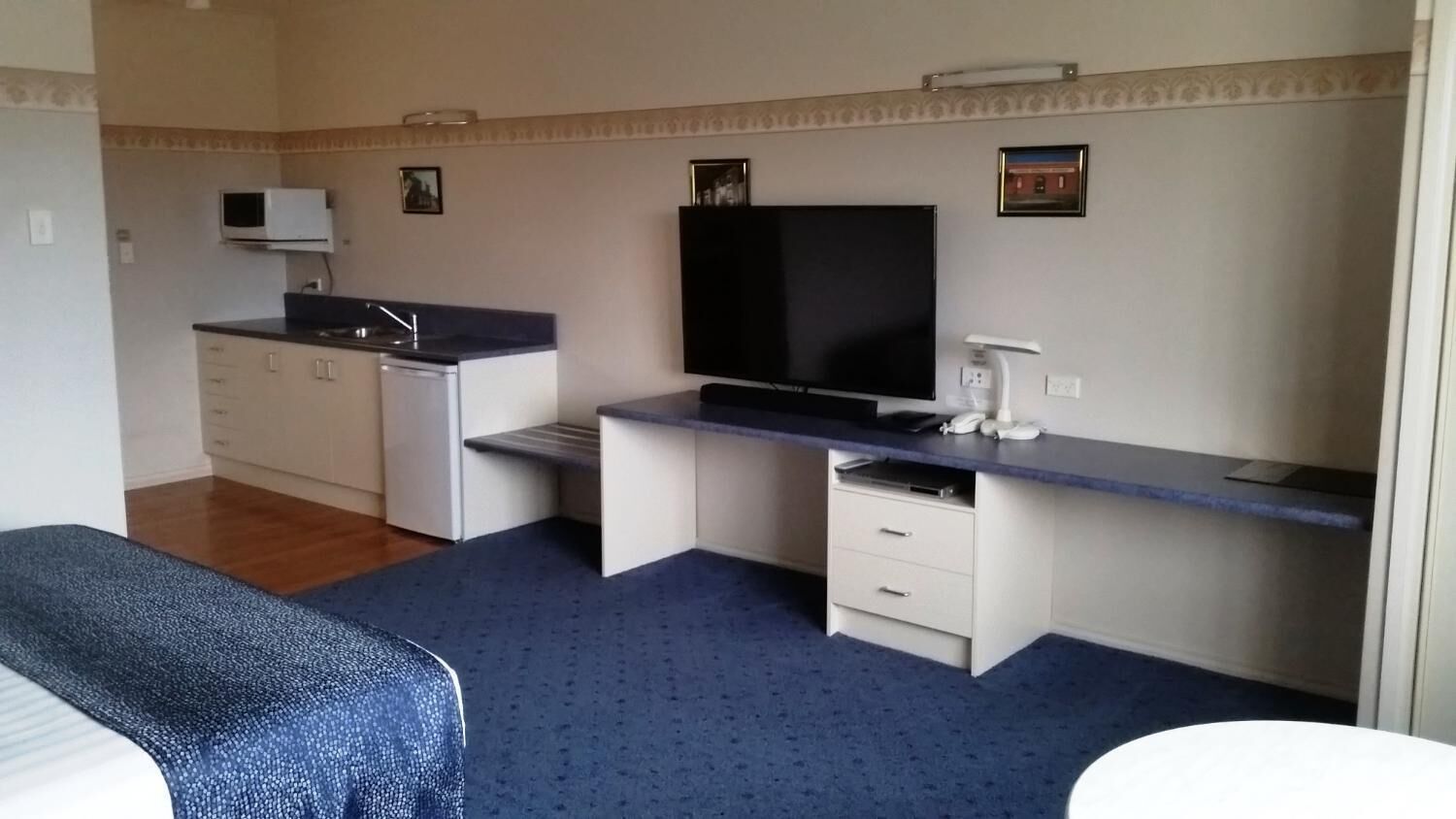 A compact room with a kitchenette, a flat-screen TV, a desk, and a bed.