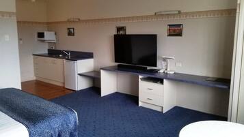 A compact room with a kitchenette, a flat-screen TV, a desk, and a bed.