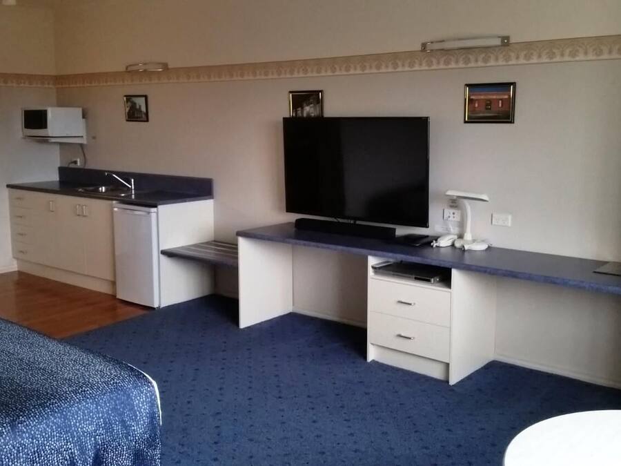 A compact room with a kitchenette, a flat-screen TV, a desk, and a bed.