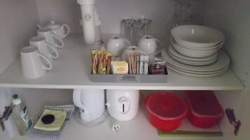 Una cocina con tazas blancas, teteras, una tetera, una cafetera y una pila de platos.