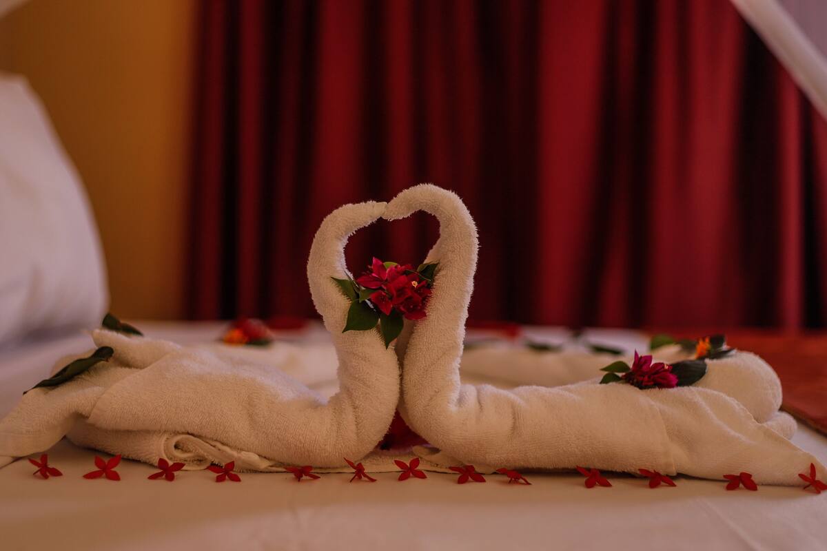 Ein Bett mit zwei handgeschöpften Schwanen aus Handtüchern, einem Strauß roter Blumen und roten Dekorationselementen.