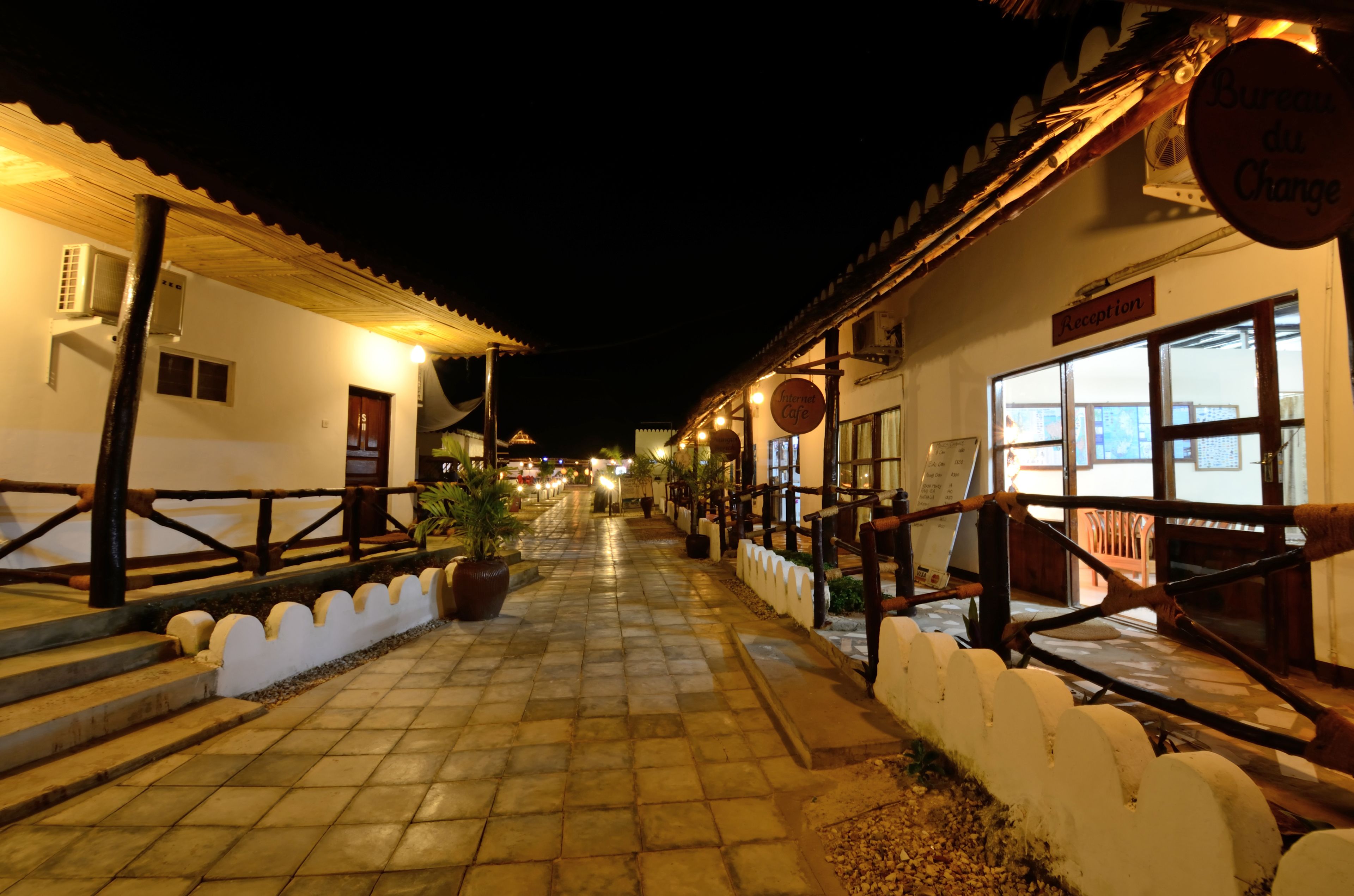 A nighttime view of a street lined with buildings, including a reception area and a sign for 'Bureau du Change'.