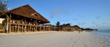 A beach with thatched-roof structures, wooden walkways, and a sandy shore.