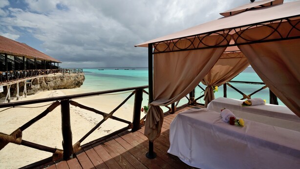 A beachside resort with a wooden deck, a covered seating area, and a view of the turquoise sea.