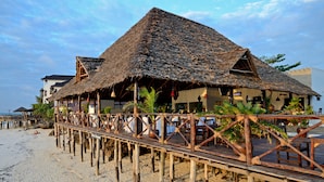 A beachside resort with thatched-roof structures, wooden walkways, and outdoor seating areas.