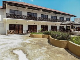 Ein zweistöckiges Gebäude mit Balkon, zahlreichen Fenstern und einer überdachten Sitzgelegenheit mit Sonnenschirmen.