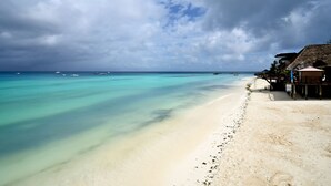 A beach with clear turquoise water, a sandy shore, and a thatched-roof building with umbrellas.