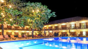 A hotel with a swimming pool, lounge chairs, and a tree.