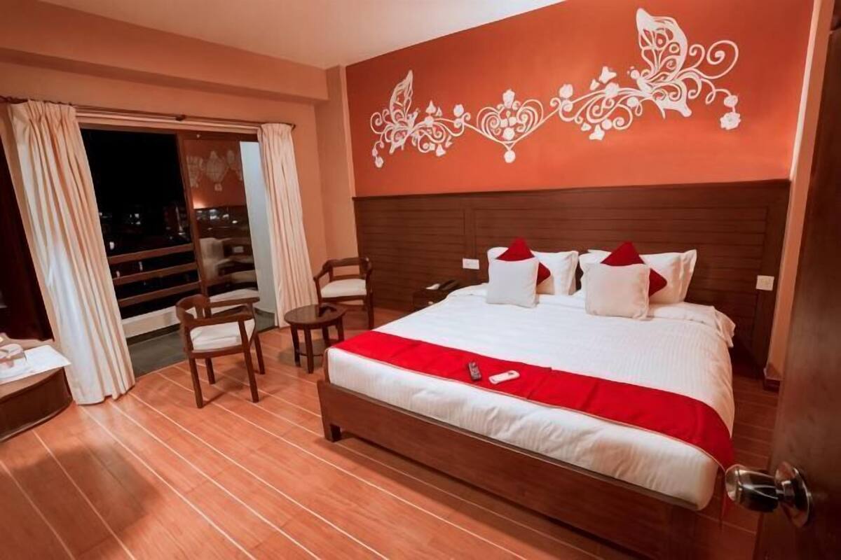 Une chambre d’hôtel dotée d’un grand lit, d’un balcon, d’un plancher en bois et d’un motif décoratif sur le mur.