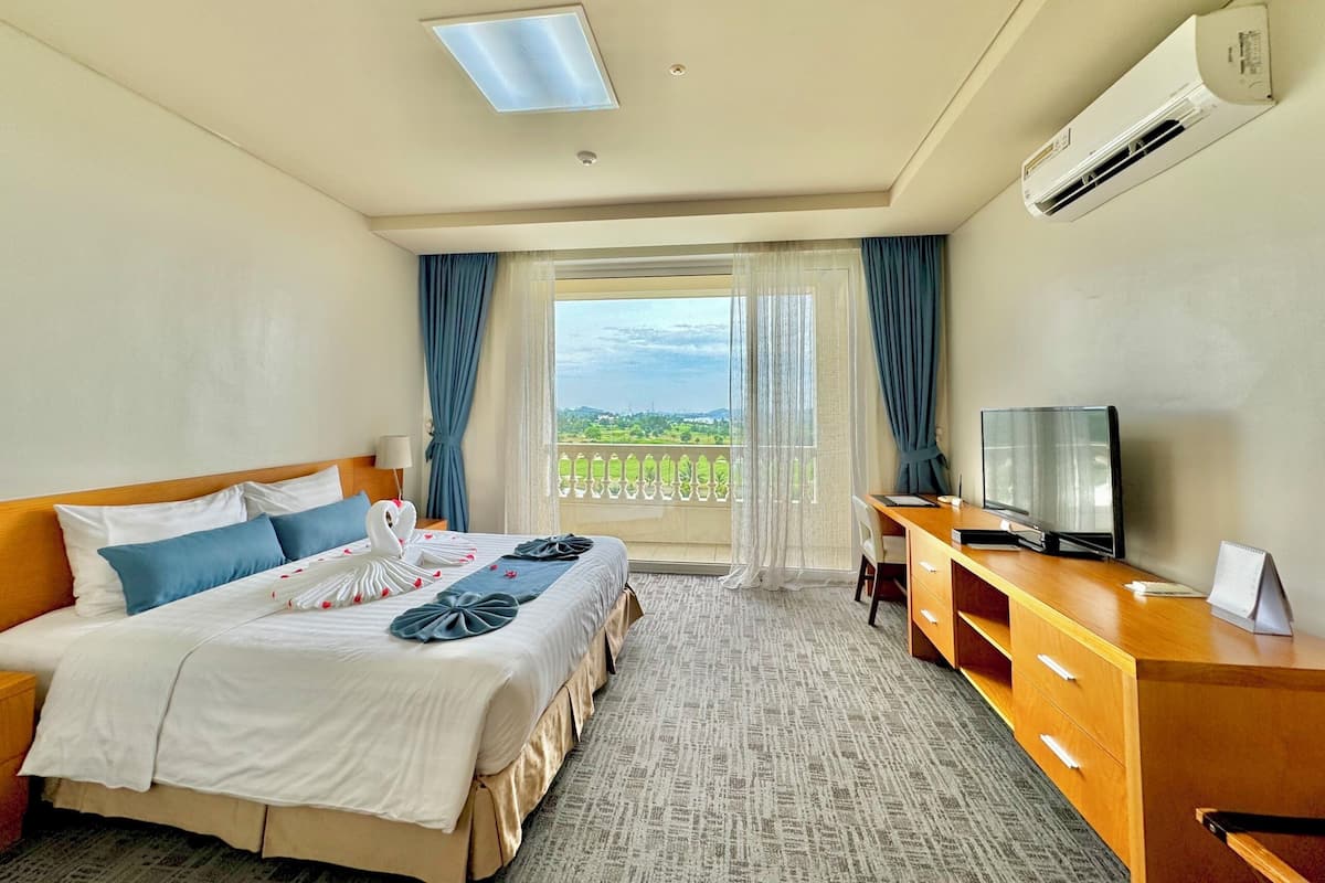 A hotel room with a bed, a desk, a TV, and a balcony with a view.