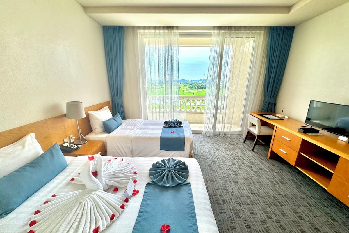 A hotel room with two beds, a desk, a TV, and a view of a golf course.