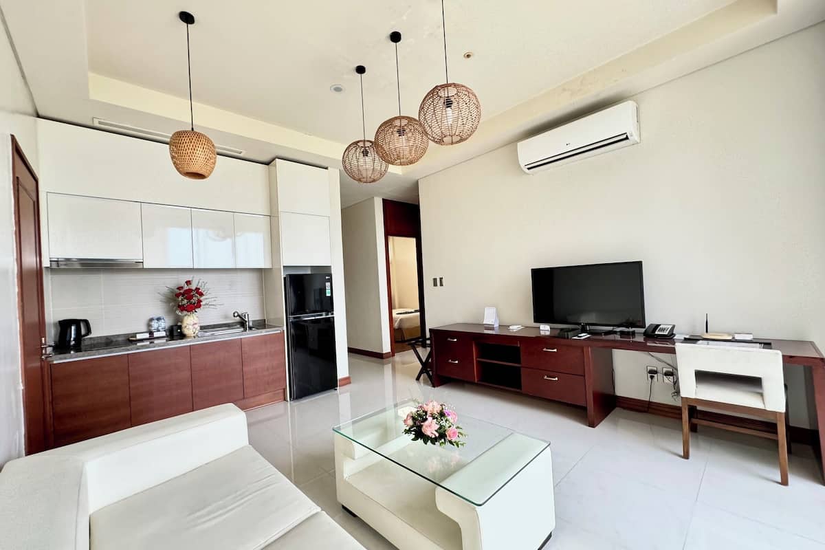A modern living room with a glass coffee table, white sofa, and a TV on a wooden desk.