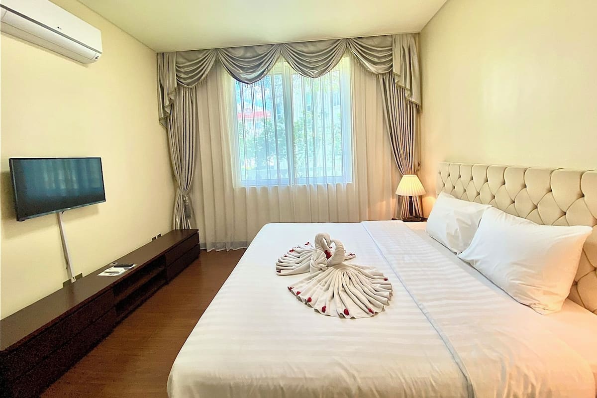 A hotel room with a bed, a TV, a desk, and a window with curtains.