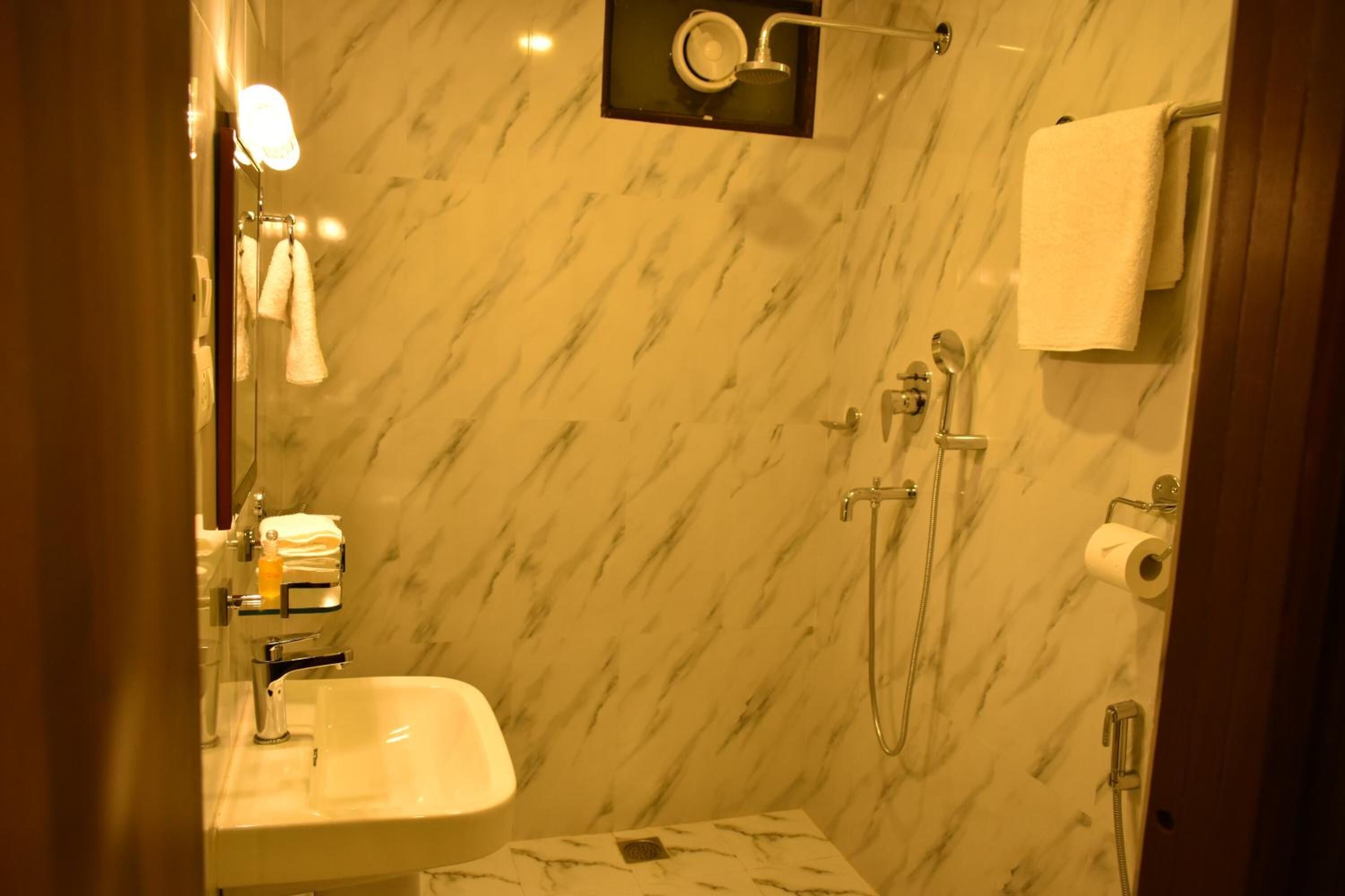 A bathroom with a marble wall, a sink, a mirror, a towel rack, and a shower area.