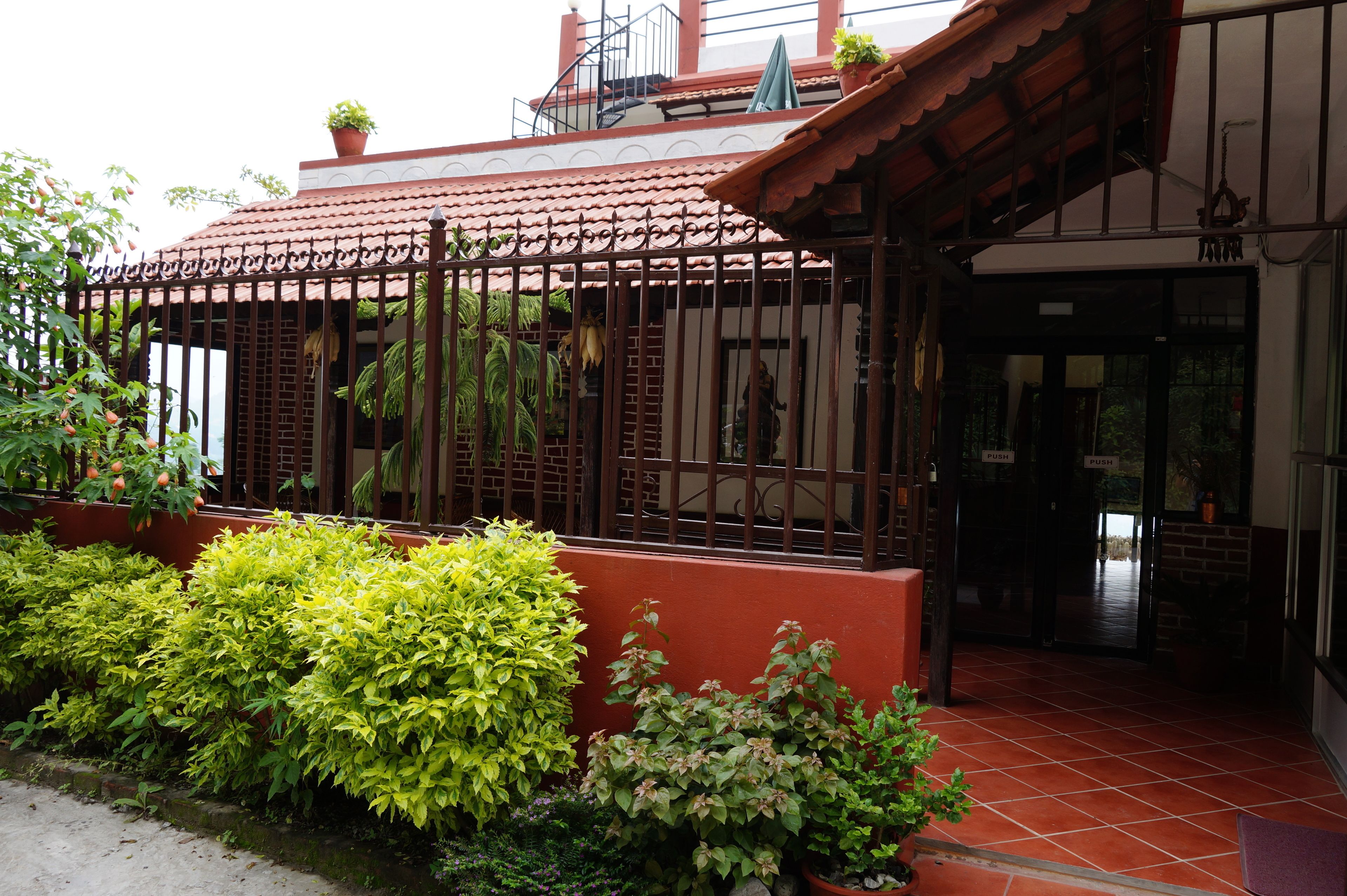 A building with a red-tiled roof, a gated entrance, and potted plants.