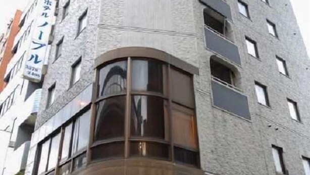 A corner building with a textured facade, multiple windows, and a sign indicating a hotel.