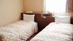 A hotel room with two single beds, a bedside table with a phone and a lamp, and a window with curtains.