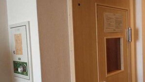 A wooden door with a small window and a handle, a wall-mounted thermostat, and a notice board.