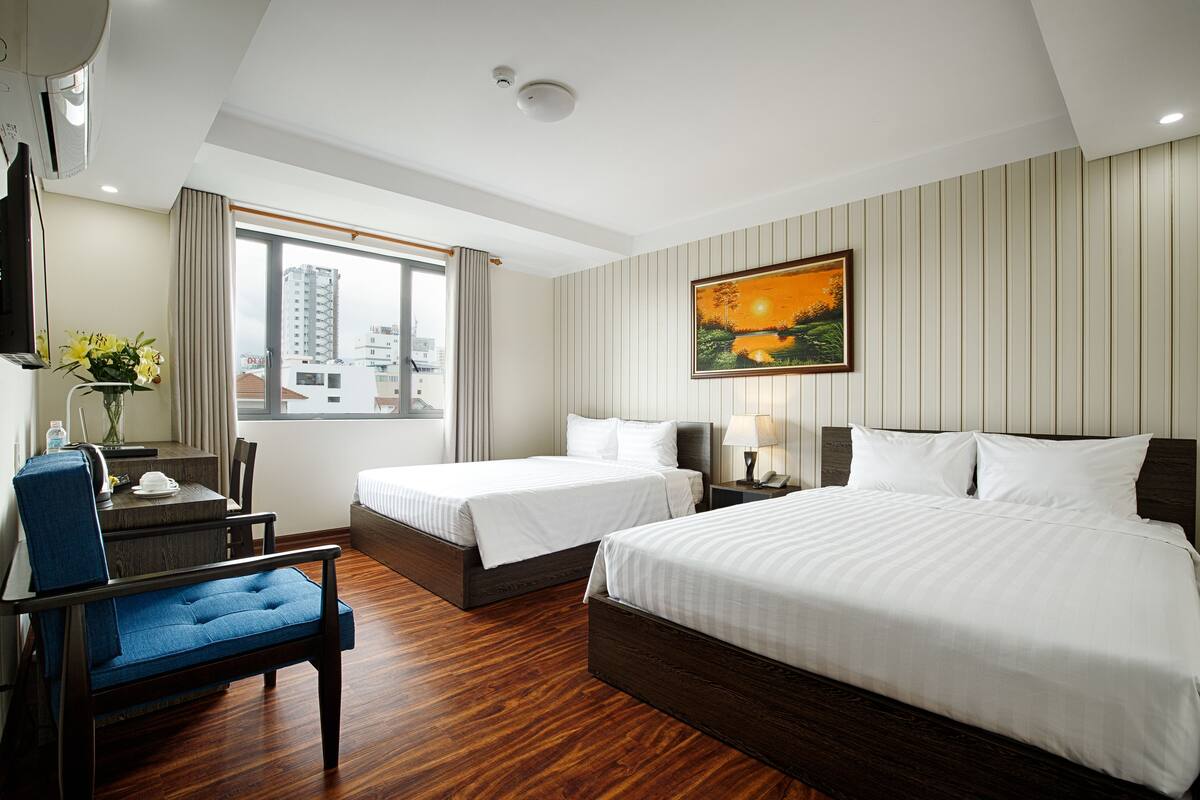 Une chambre d’hôtel avec deux lits, un bureau avec une chaise, une télévision et une fenêtre avec des rideaux.