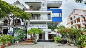 Un hôtel de charme à la façade blanche et bleue, doté d’un balcon et agrémenté de plantes en pot dans la cour.
