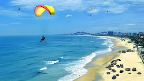 Une plage où l’on peut voir plusieurs parapentes et une personne en train de faire du parapente.