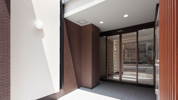 A modern building entrance with a glass door, a brick wall, and a tiled floor. - HOTEL.LINKS Dobutsuen-mae (Osaka)