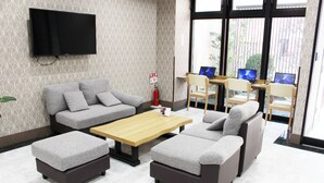 A modern living room with a grey sofa, matching ottomans, a wooden coffee table, and a flat-screen TV mounted on the wall. - HOTEL.LINKS Dobutsuen-mae (Osaka)