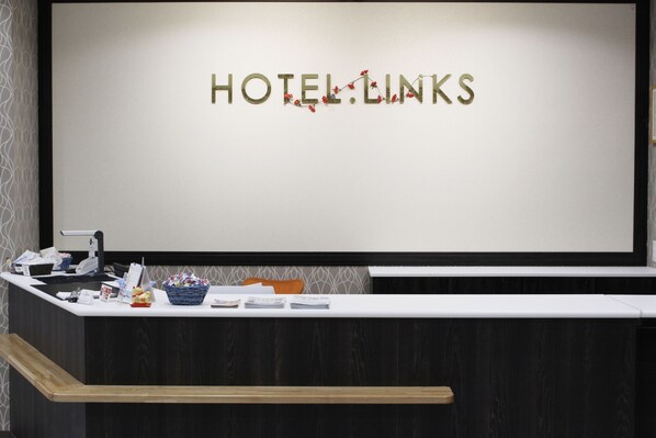 A reception desk with a sign reading "HOTEL LINKS" and a counter with various items including a basket, a phone, and some papers.