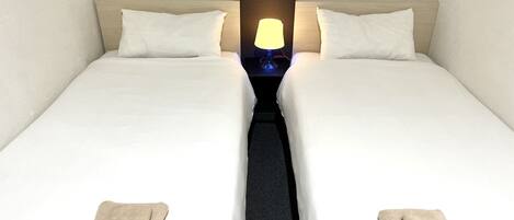 Une chambre d’hôtel avec deux lits simples, une table de chevet avec une lampe et deux serviettes sur le sol.