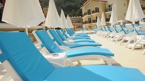 Une rangée de chaises longues bleues et blanches, surmontées de parasols blancs, disposées au bord d’une piscine.