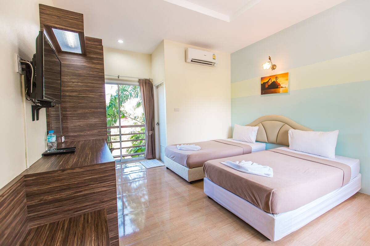A hotel room with two beds, a TV, an air conditioner, and a view of greenery.
